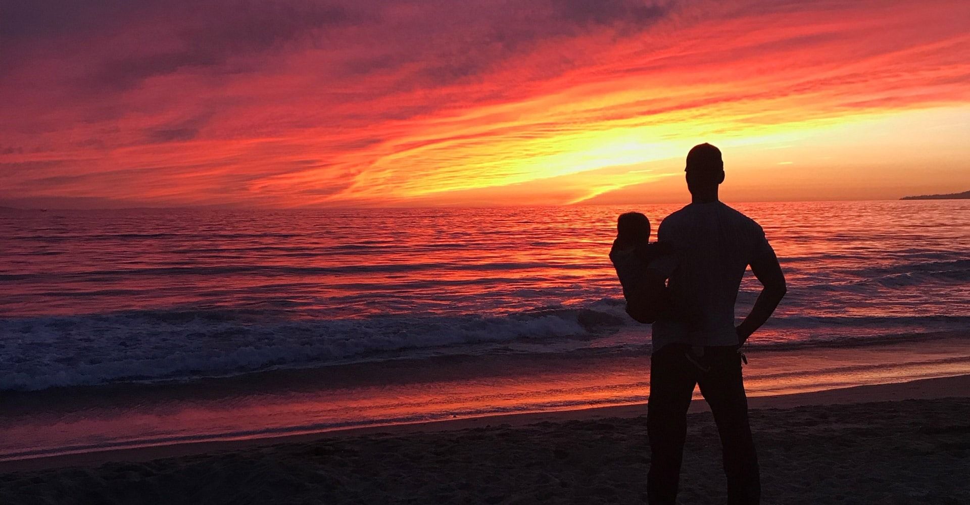 Man holding child standing on the beach at sunset