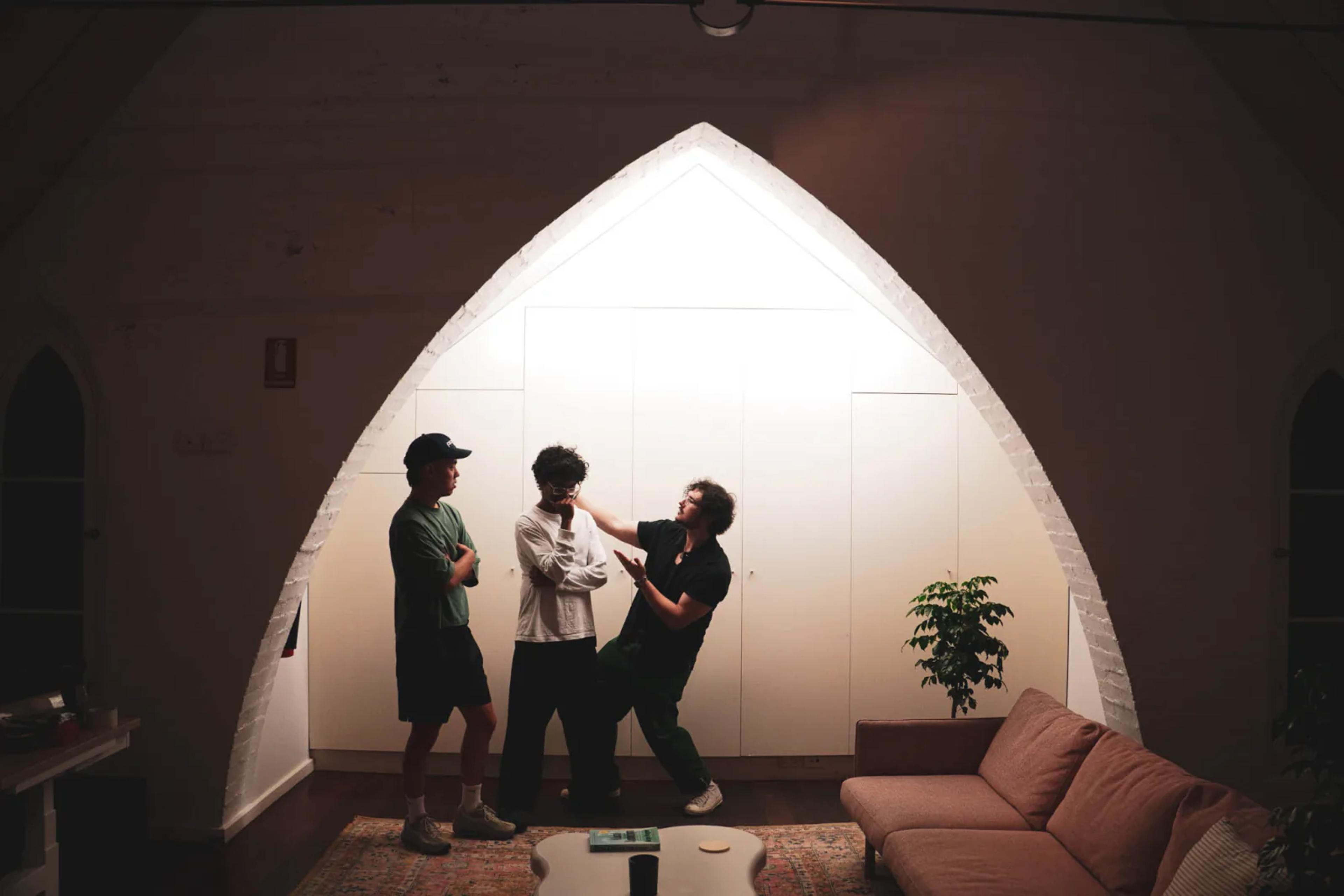 Three people chatting under the tall white gothic arch of Broad Church's converted-church interior, beside a sofa and plant