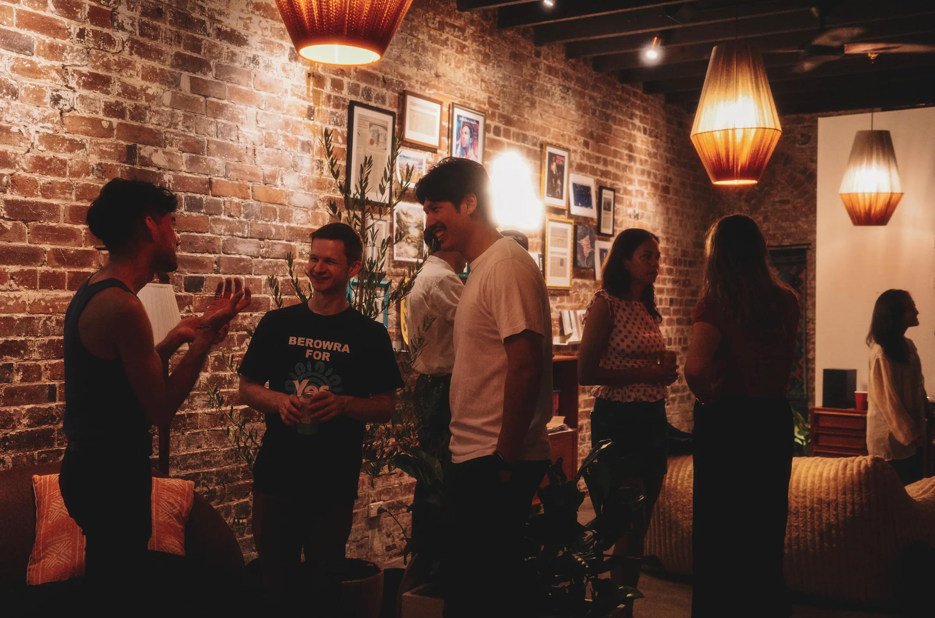 Guests chatting at Broad Church — exposed-brick walls, framed art and woven pendant lamps