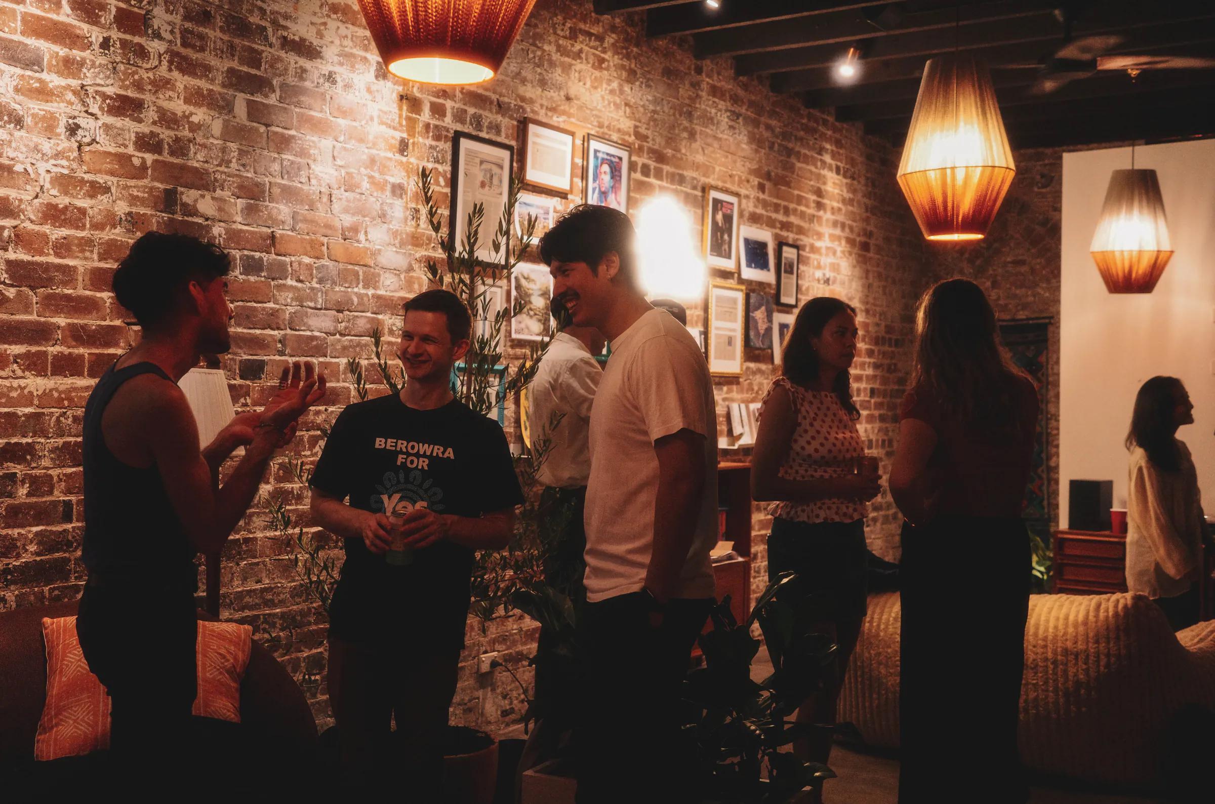 Guests chatting at Broad Church — exposed-brick walls, framed art and woven pendant lamps