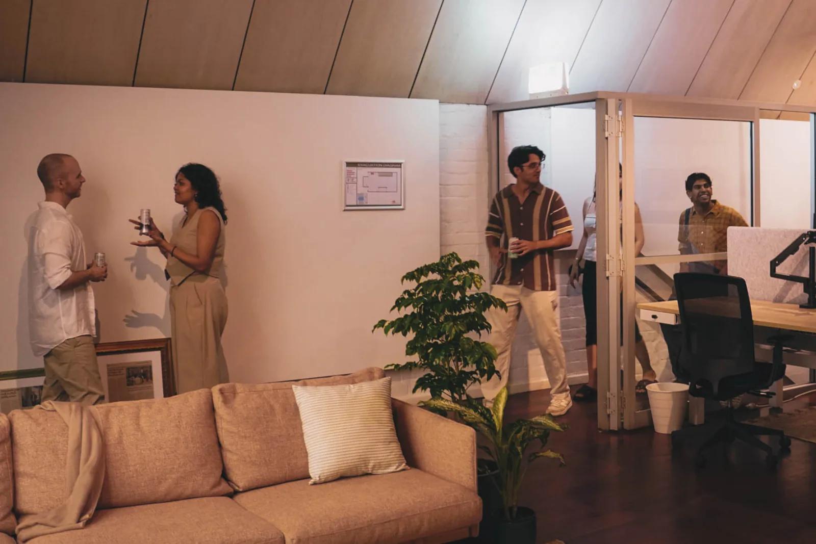 Guests mingling with drinks in Broad Church's lounge and glass-walled co-working area, with desks and plants