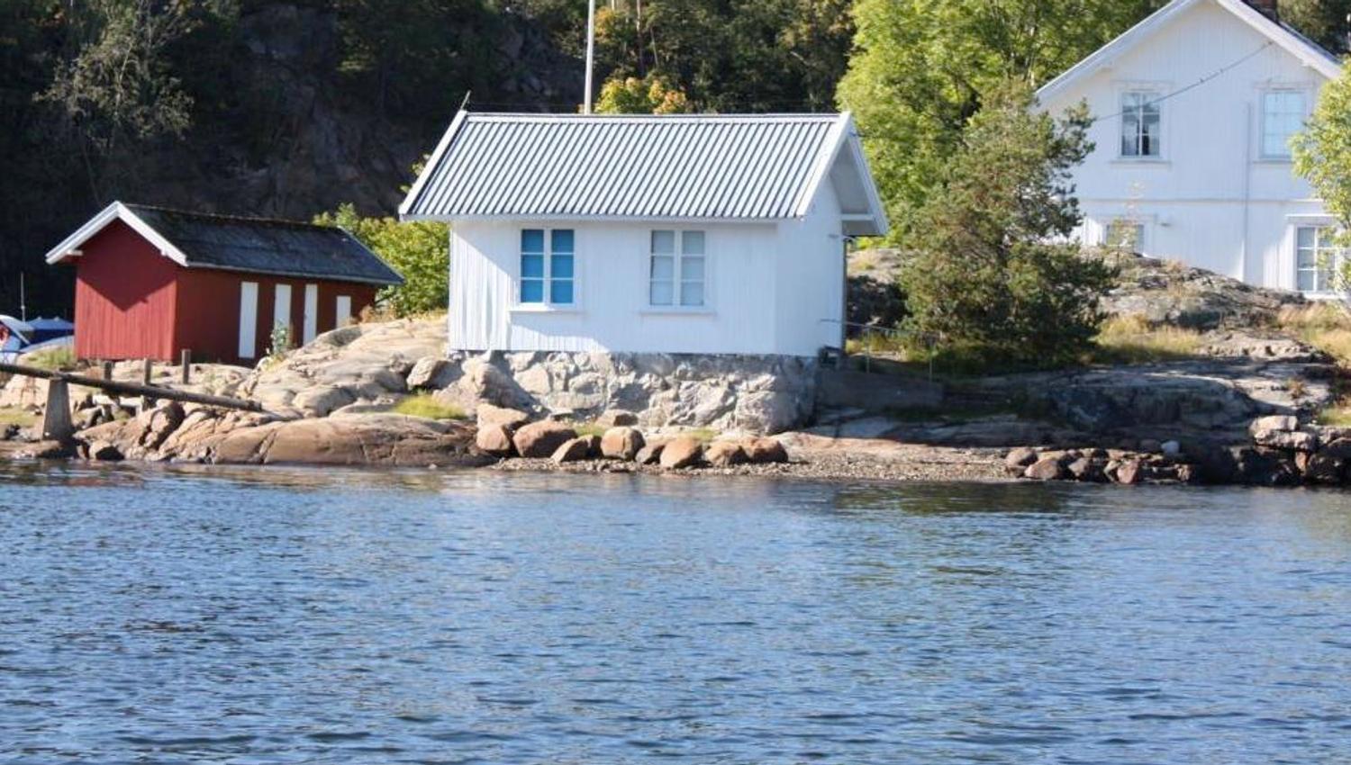 Hvitt anneks i sjøkanten og hytte bak
