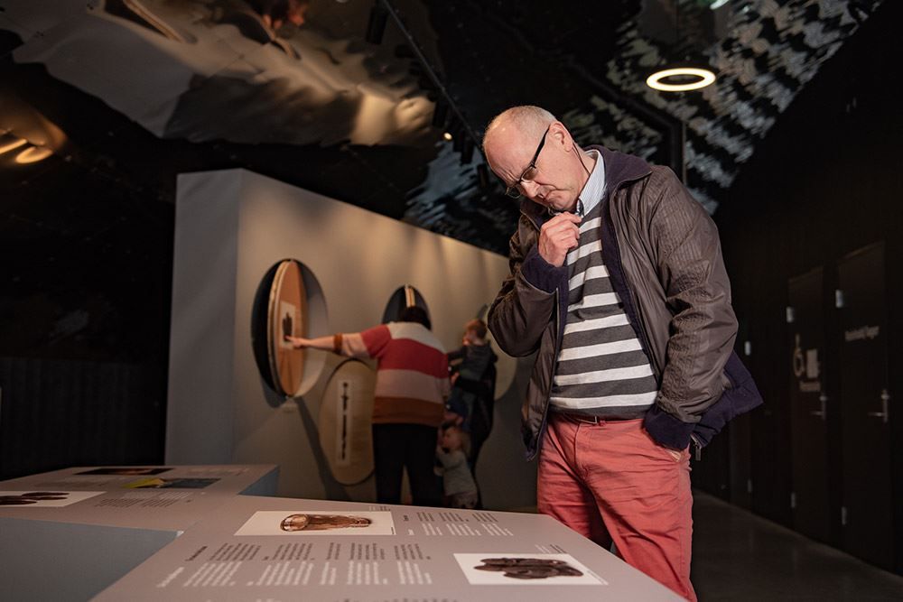 Besøkande les informasjon og lærer om vikingane på Sagastad. Informasjonstavle i ei mørk museumutstilling, med andre besøkande i bakgrunnen..