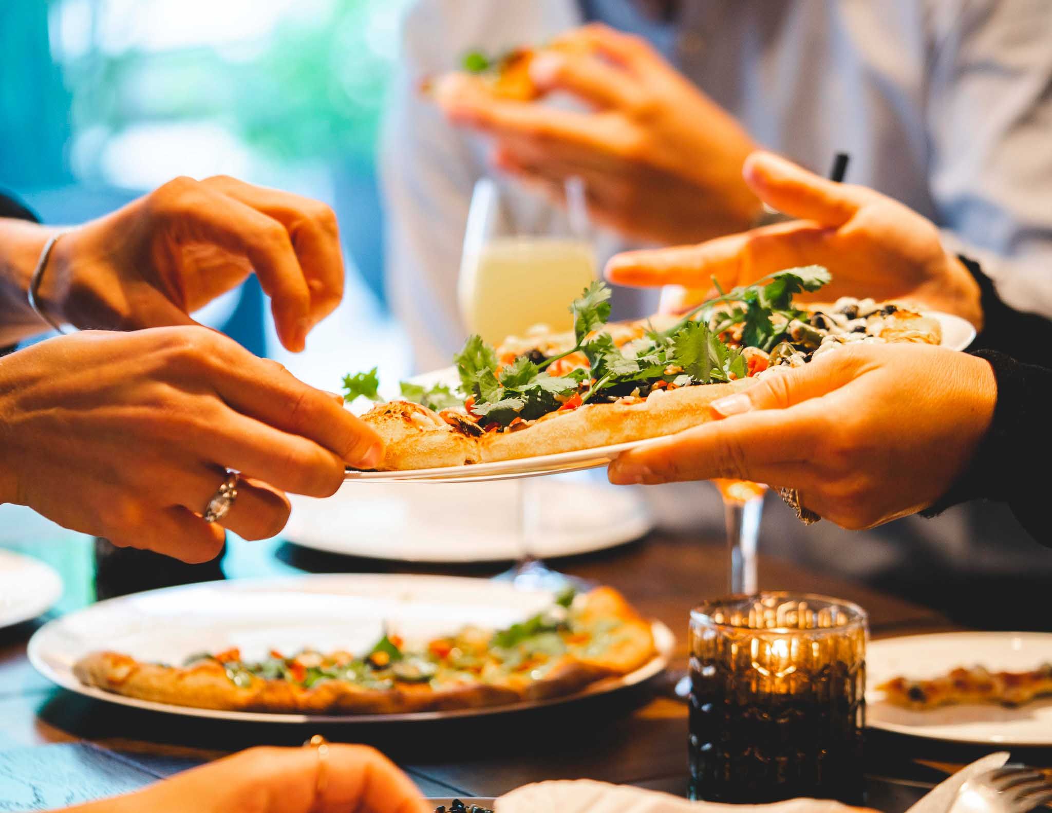 Pizzaer på bord og som sendes fra et sett med hender til et annet