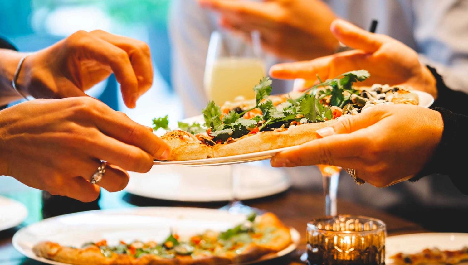 Pizzaer på bord og som sendes fra et sett med hender til et annet