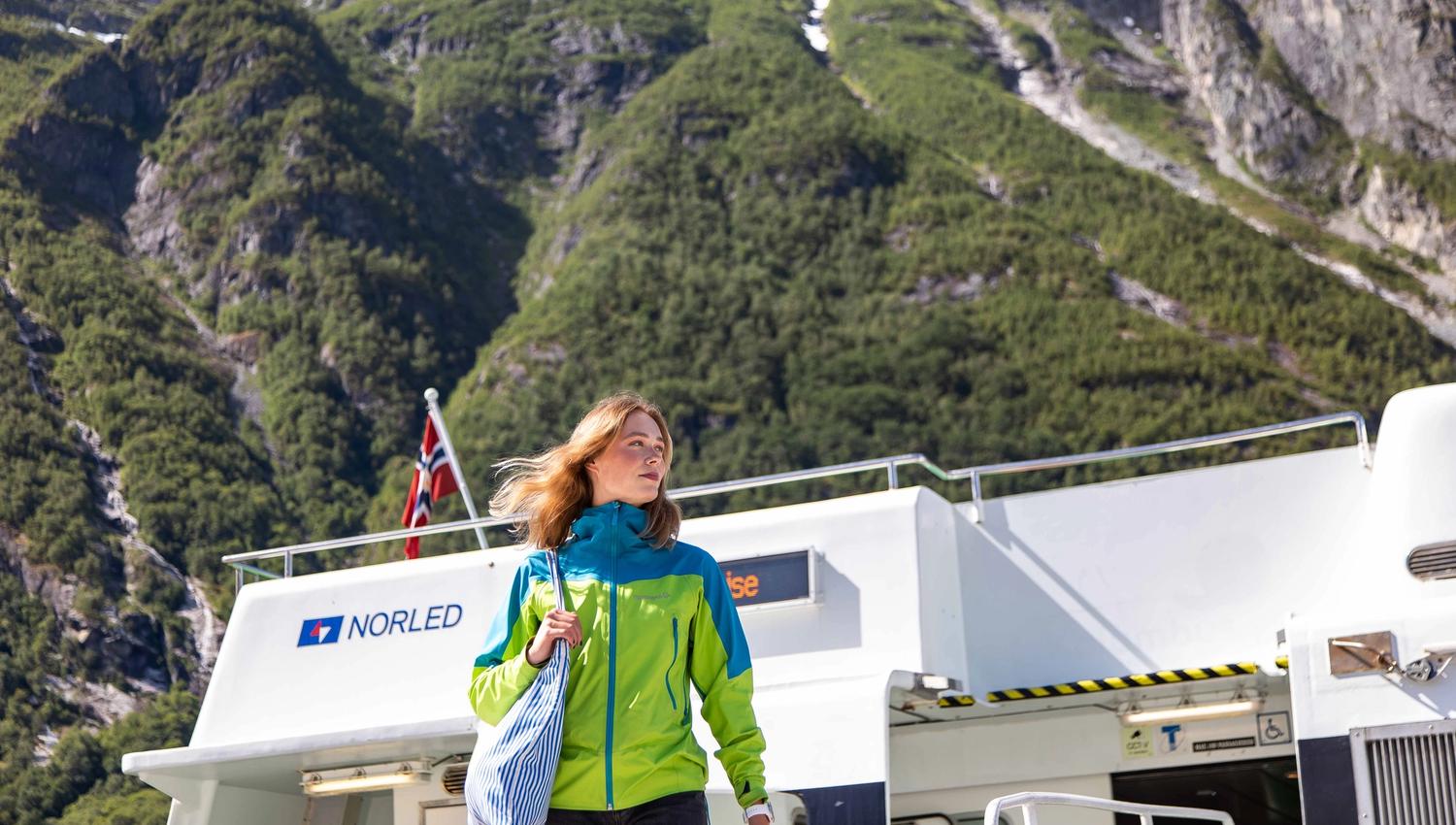 Ung turist går av båten i Eidfjord med flotte fjell i bakgrunnen.