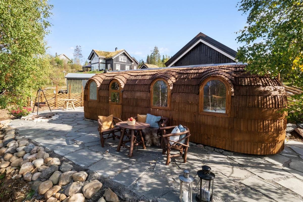 Wooden cabin pods with seating area and stone patio in summer sunlight.