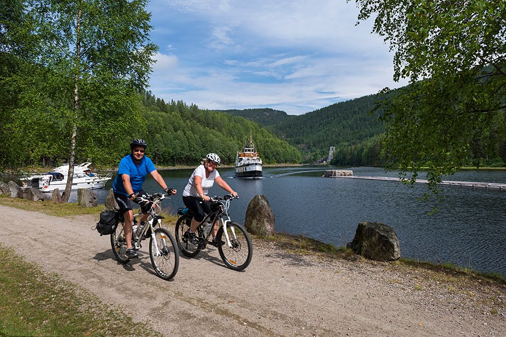 couple is bicycling along the Telemark Canal with MS Victoria in the background 