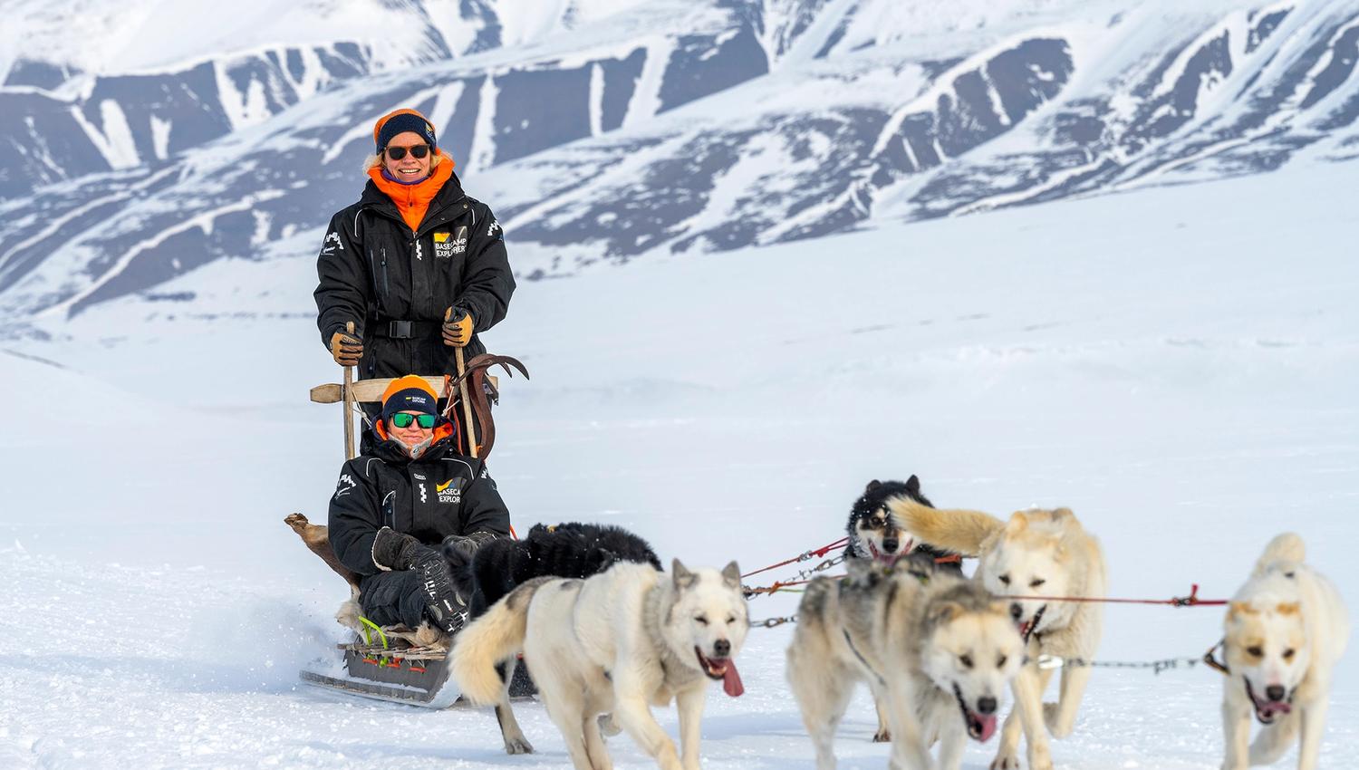 Two guests dog sledding with a team of sled dogs in front of them.