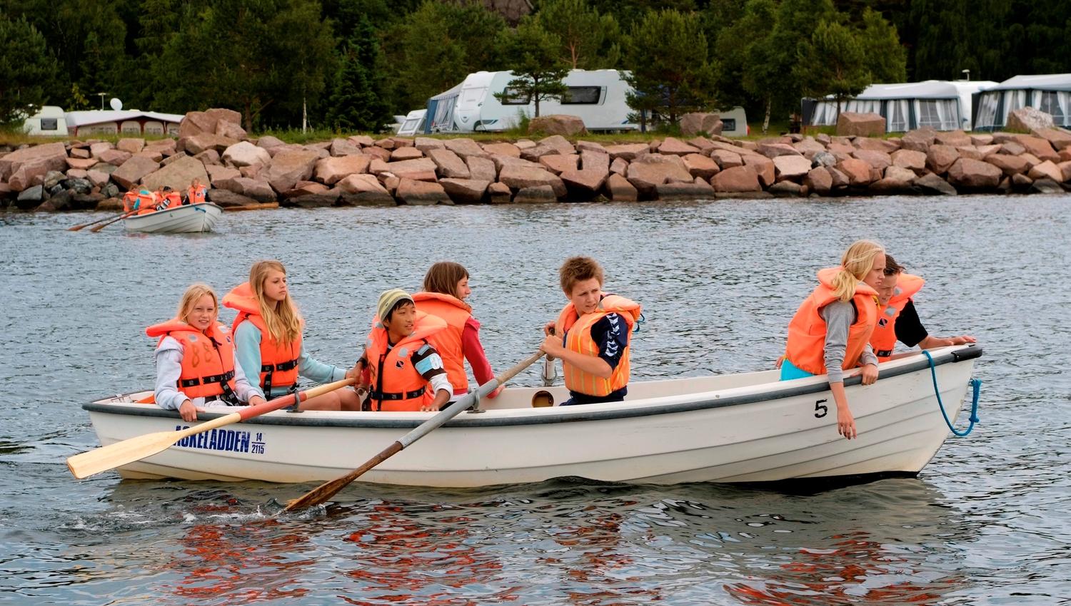 Barn som er ute i robåt på vannet utenfor campingplassen
