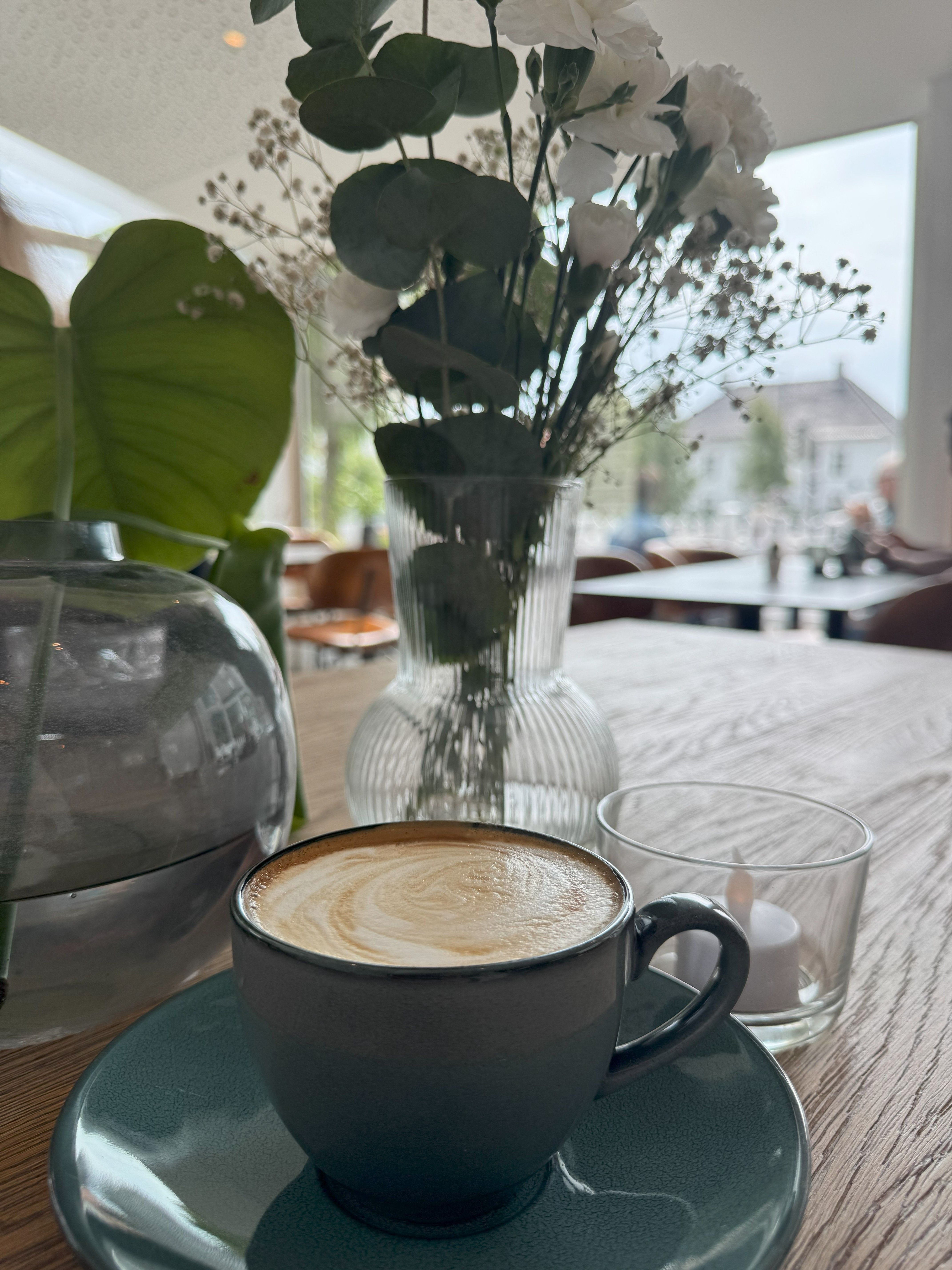 En kopp cappuccino og blomster på bordet på Herlighed