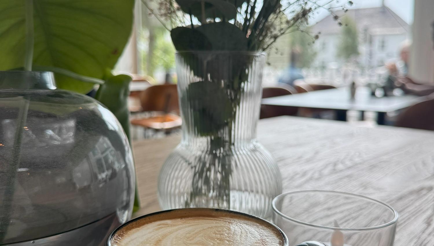 En kopp cappuccino og blomster på bordet på Herlighed