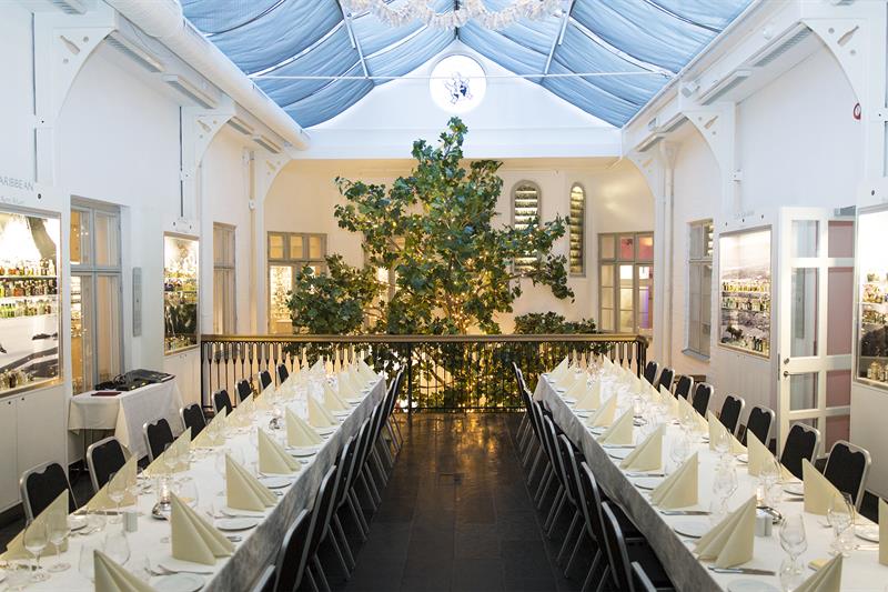 Festsalen med to langbord med hvit duk og et stort tre i bakgrunnen