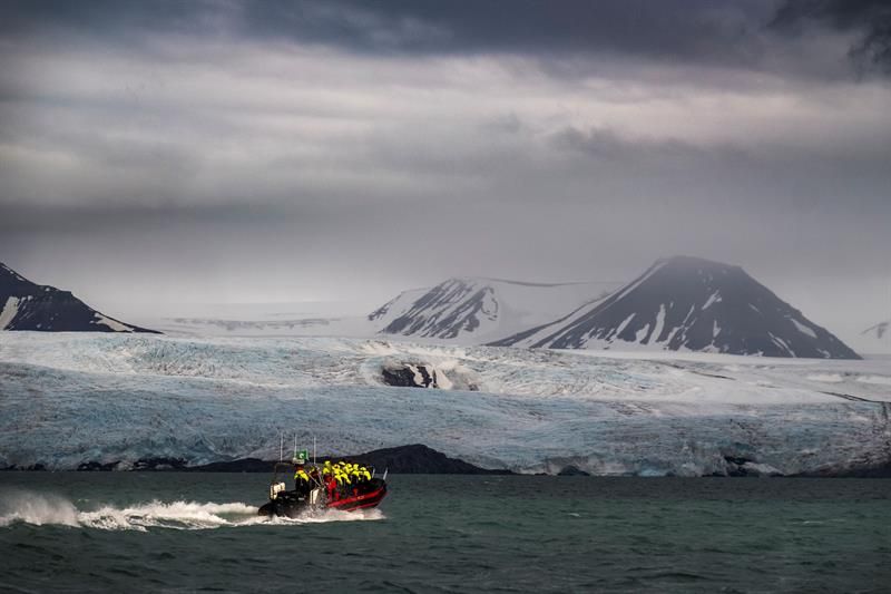 RIB-båt foran isbre under dramatiske skyer.