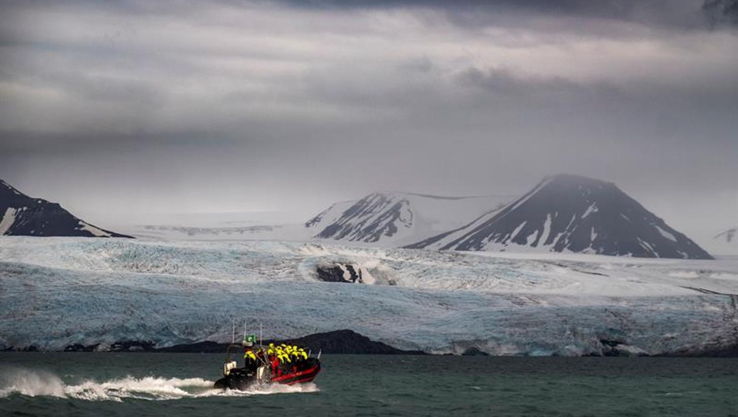 RIB-båt foran isbre under dramatiske skyer.