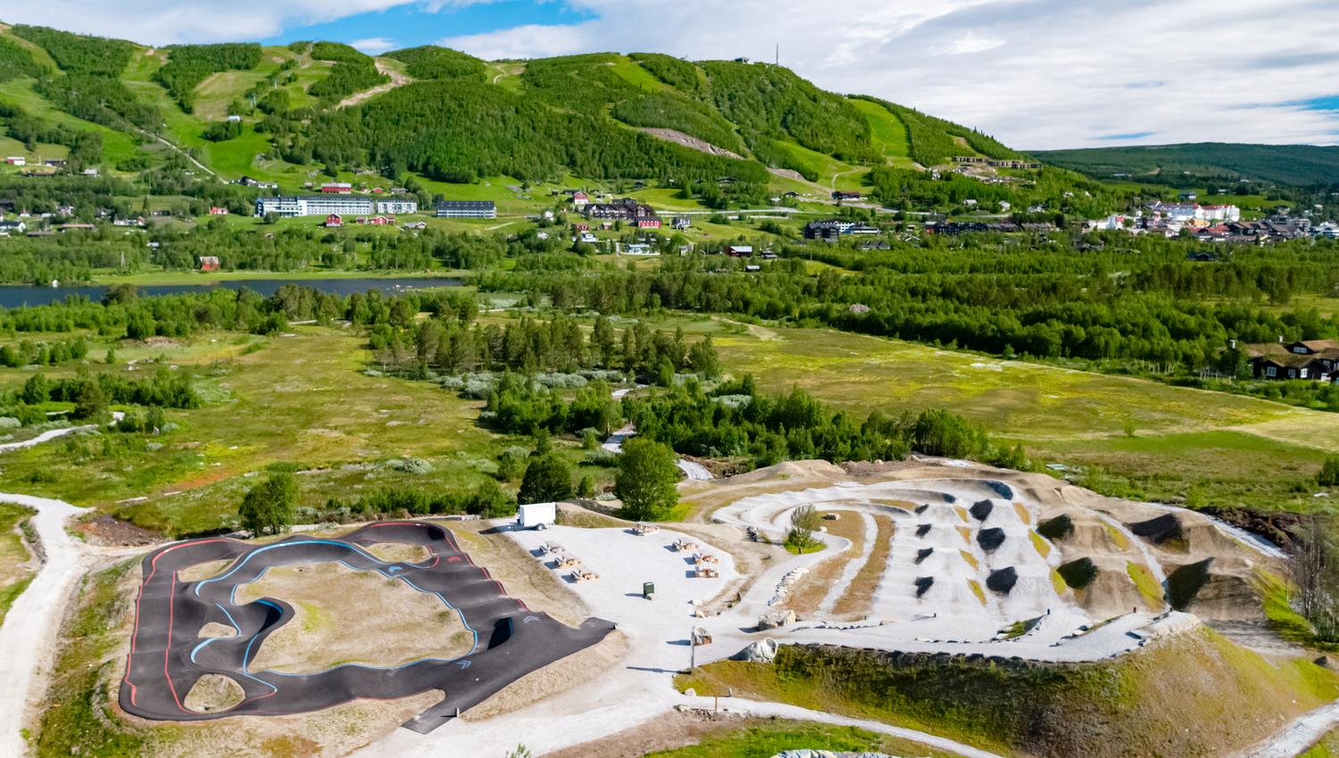Vestlia Sykkelpark på Geilo med pumptrack og hopplinjer og grønne alpinbakker og Geilo sentrum i bakgrunn.