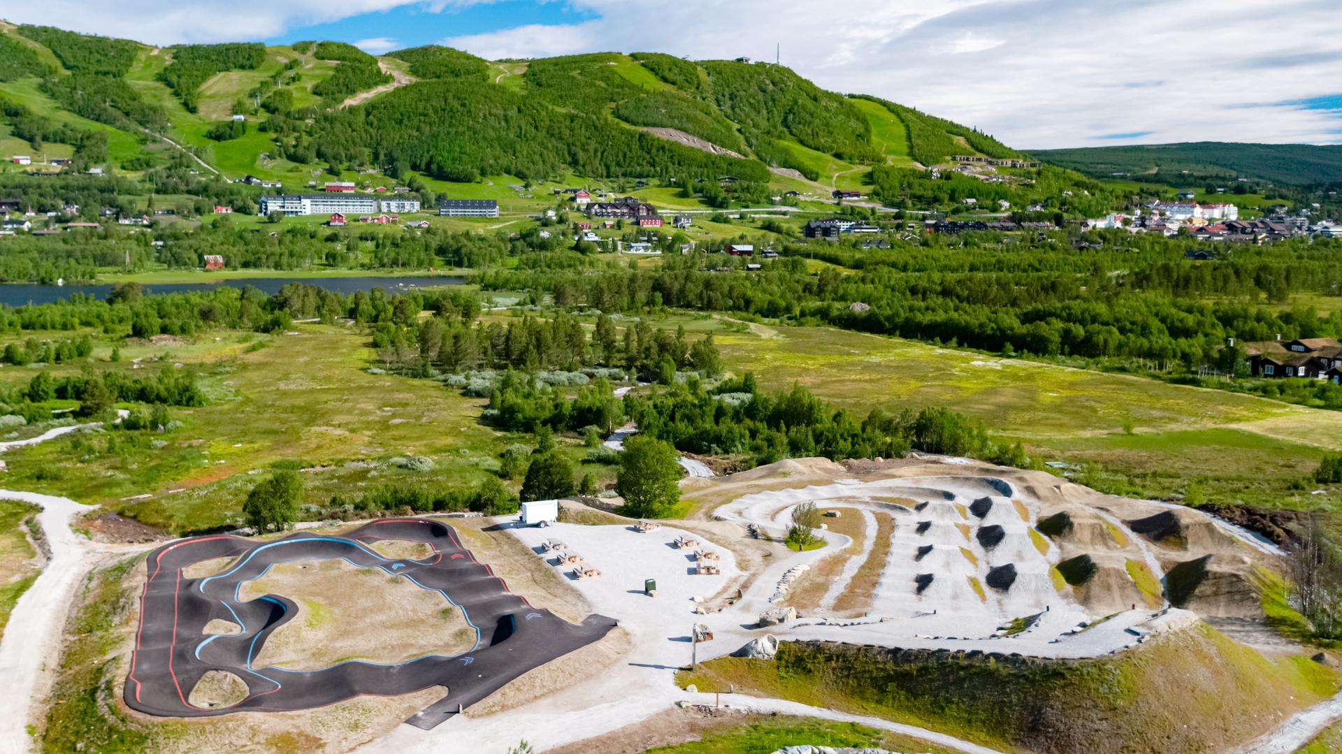 Vestlia Sykkelpark på Geilo med pumptrack og hopplinjer og grønne alpinbakker og Geilo sentrum i bakgrunn.