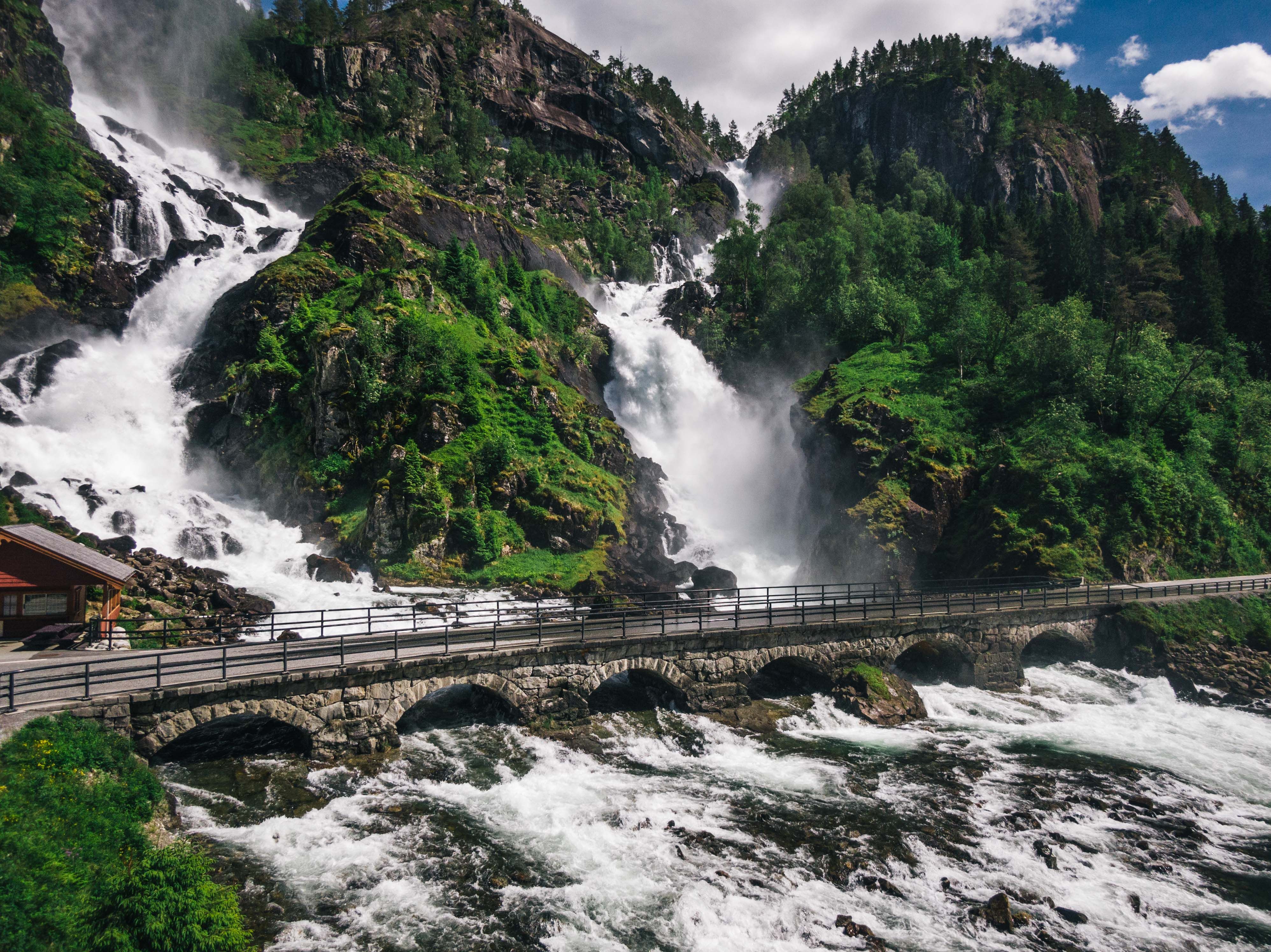 Mektige Låtefoss med en bro over den brusende elven omgitt av frodig vegetasjon.