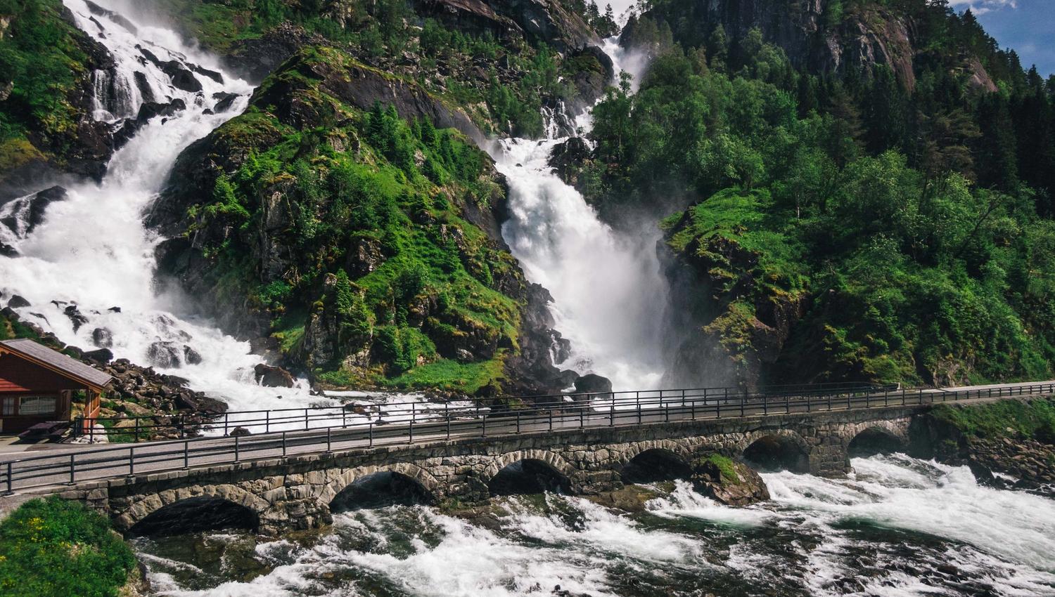 Mektige Låtefoss med en bro over den brusende elven omgitt av frodig vegetasjon.