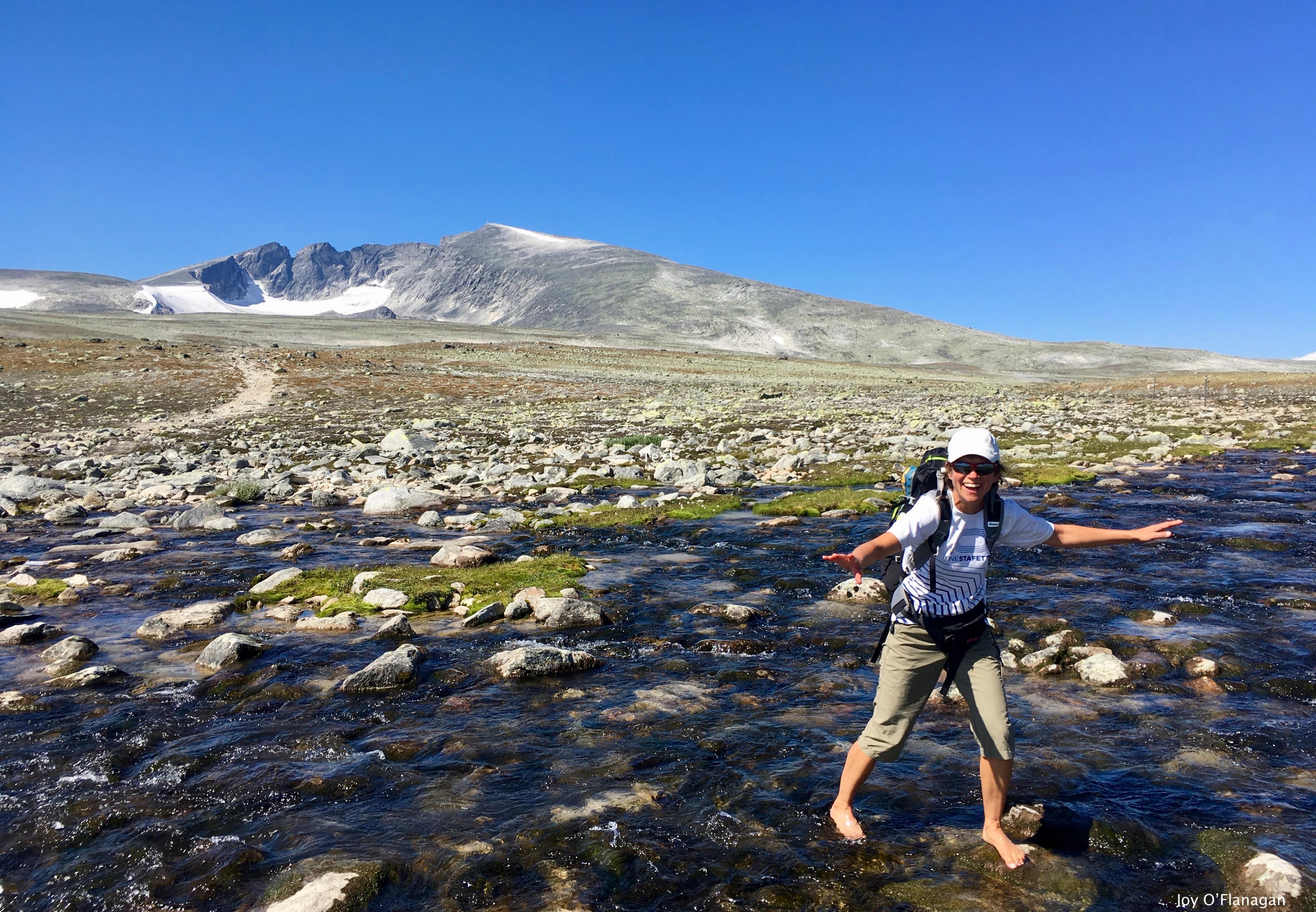 Female hiker crossing river, Snøhetta in background | Venabu Fjellhotell