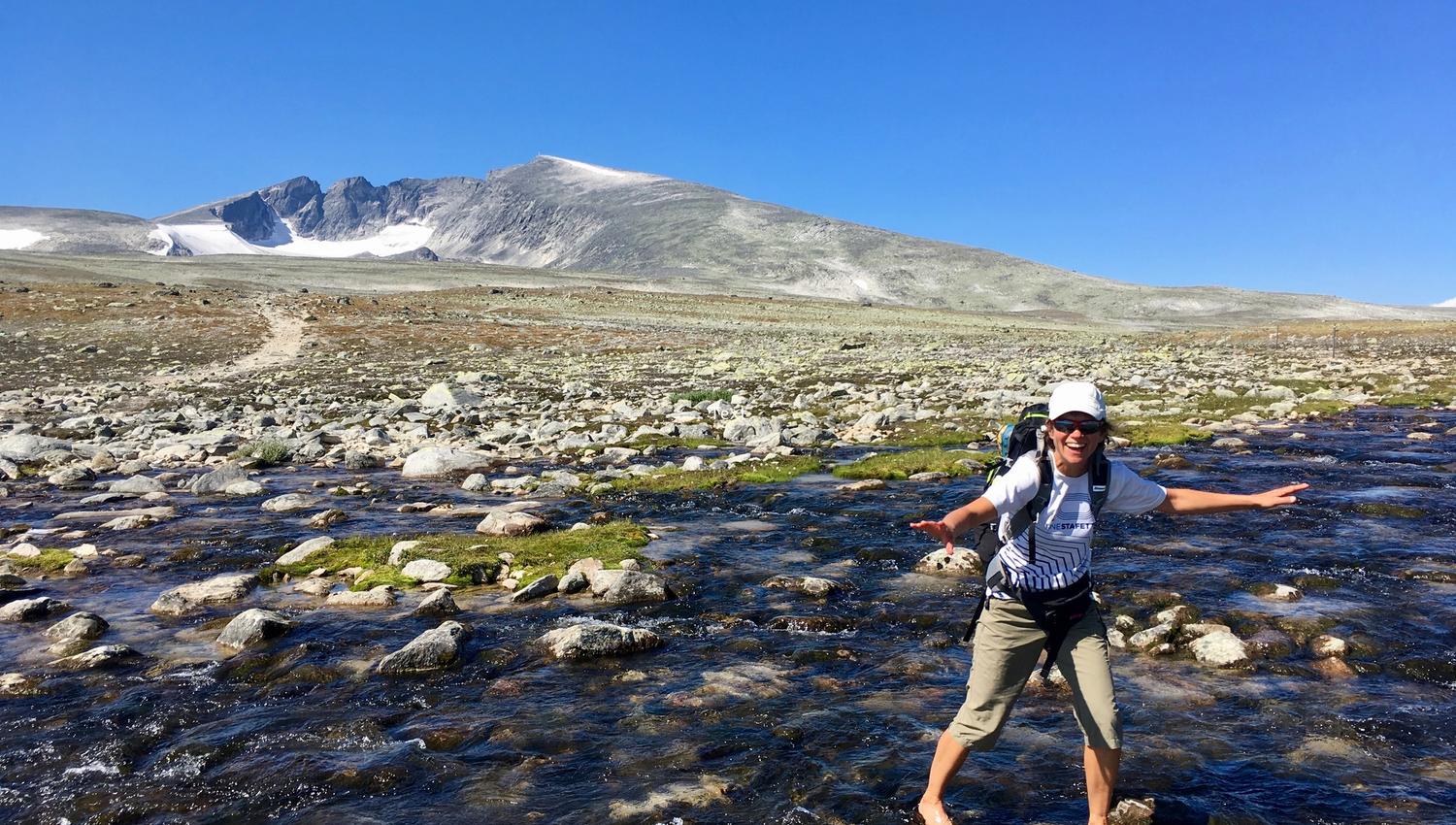 Female hiker crossing river, Snøhetta in background | Venabu Fjellhotell