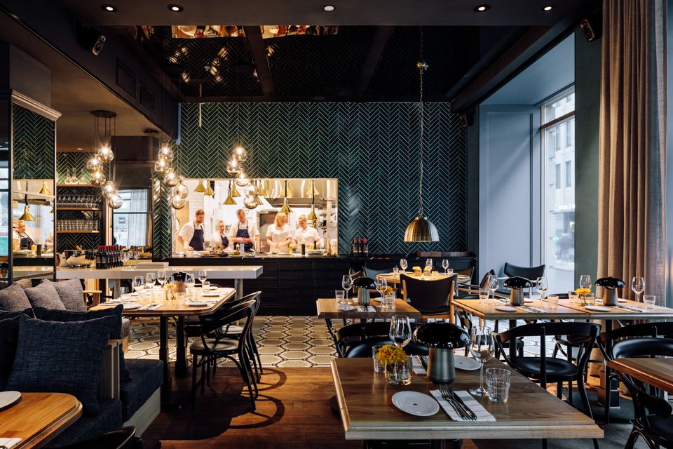 Restaurant Atlas - interiørbilde. Dekkede bord med stoler, sitteseksjon, hengende taklamper og kjøkken i bakgrunnen.