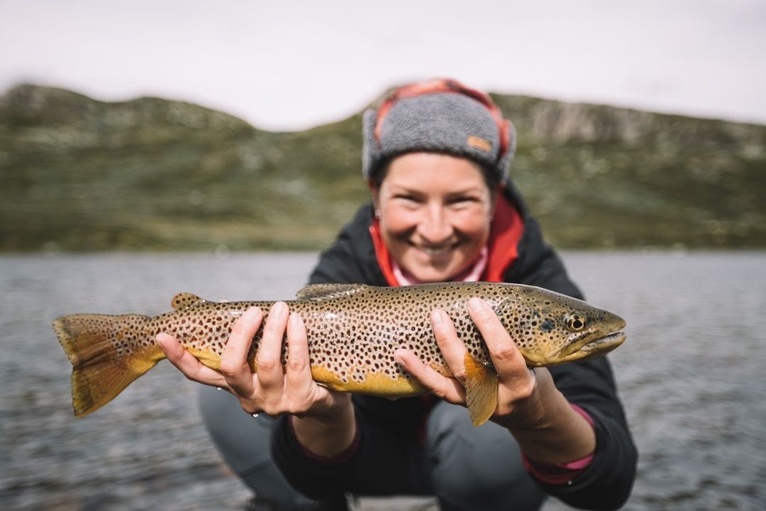 Hilde from Vinternatt is holding a trout with Mountain in the background.