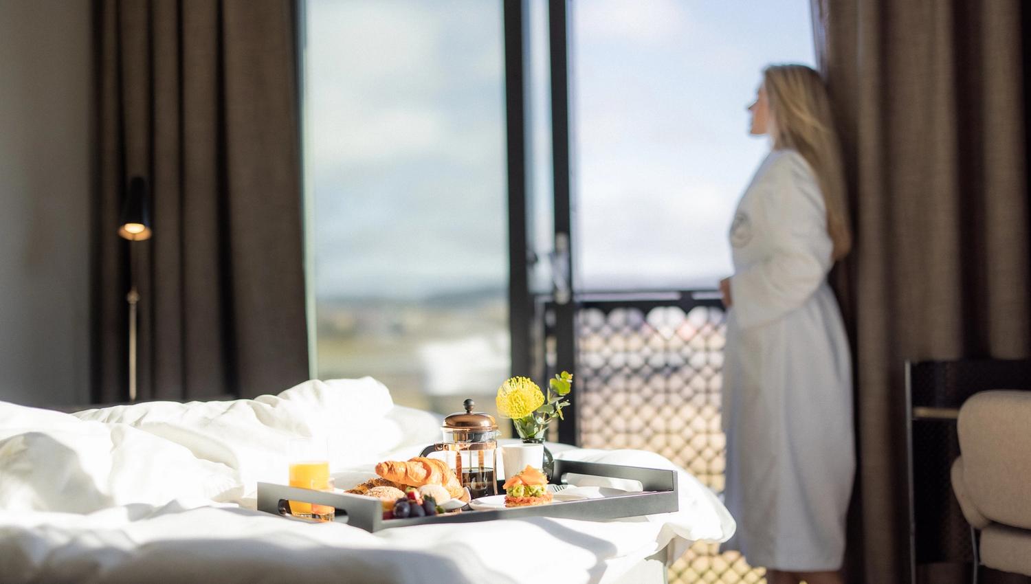 Lady looking out of å window breakfast tray on the bed