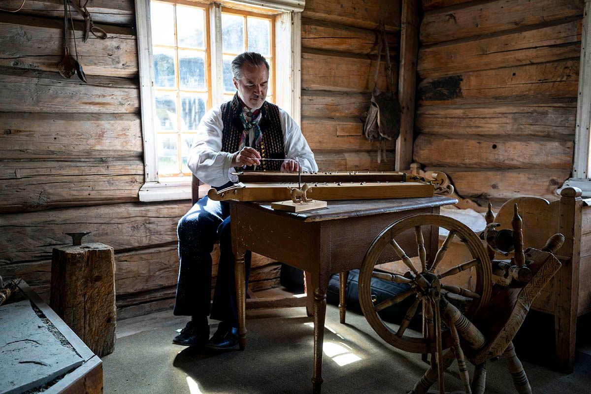 Mann spiller langeleik inne i et gammelt hus.