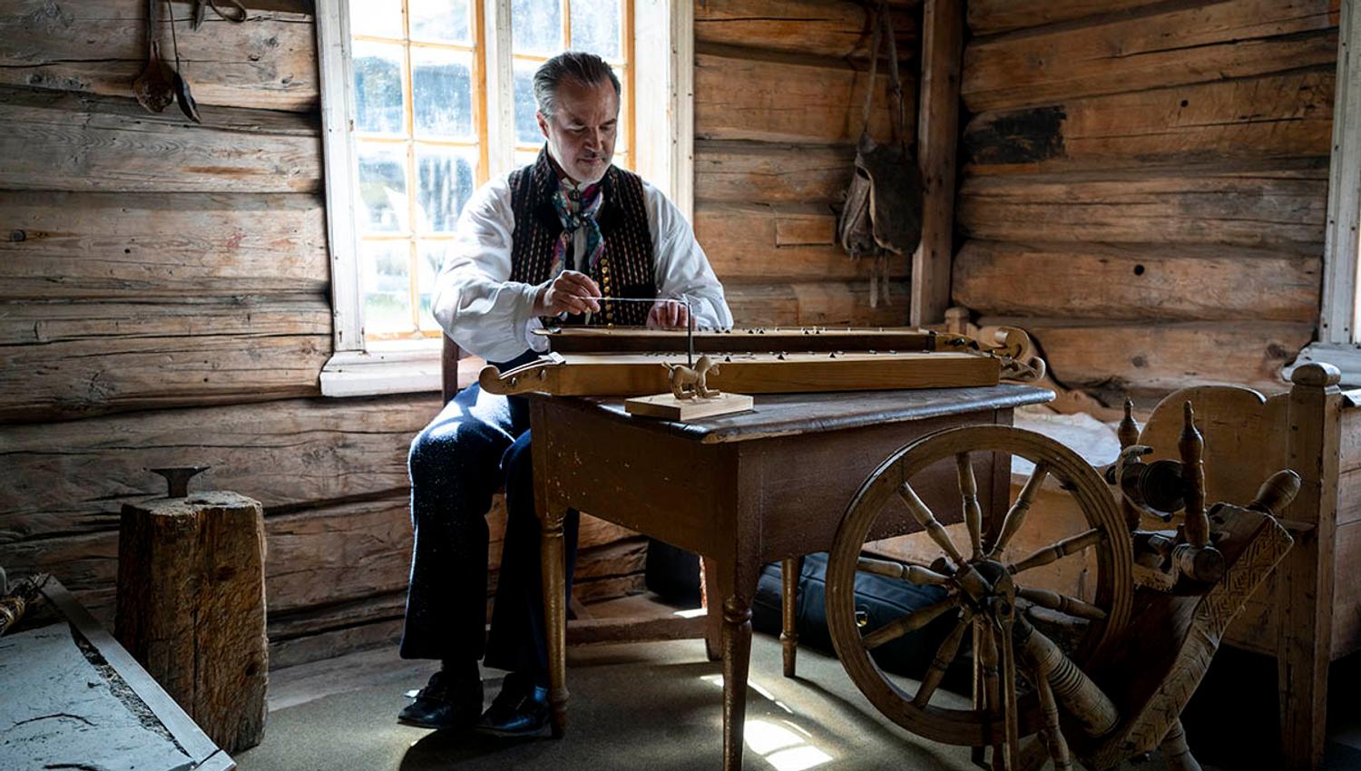 Mann spiller langeleik inne i et gammelt hus.