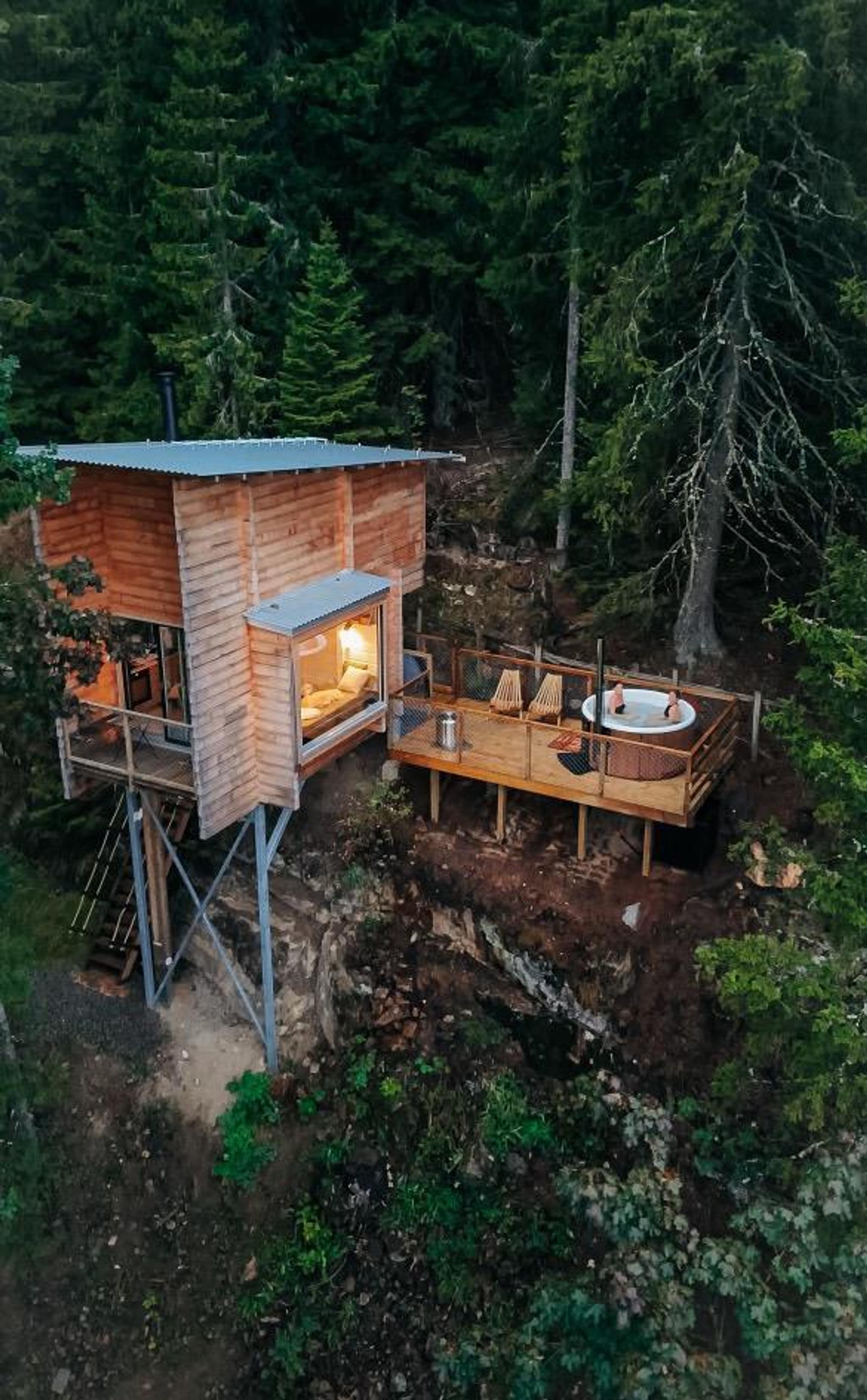 Small wooden cabin on stilts surrounded by forest, with landscape visible in the background.