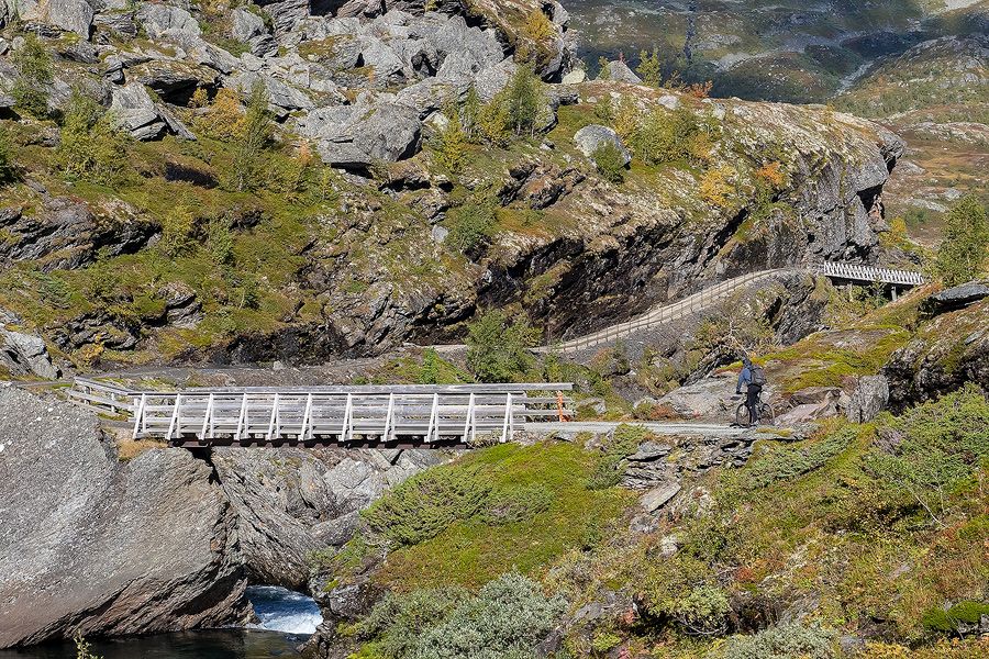 Syklist kryssar trebru på Rallarvegen i Hardanger omgitt av stein og fjell.