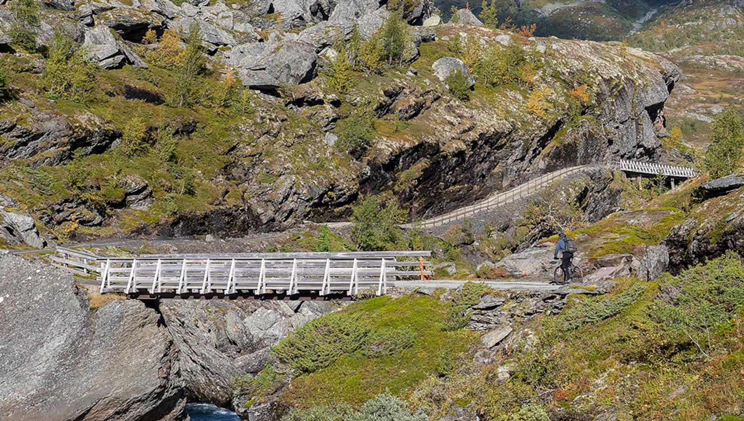 Syklist kryssar trebru på Rallarvegen i Hardanger omgitt av stein og fjell.