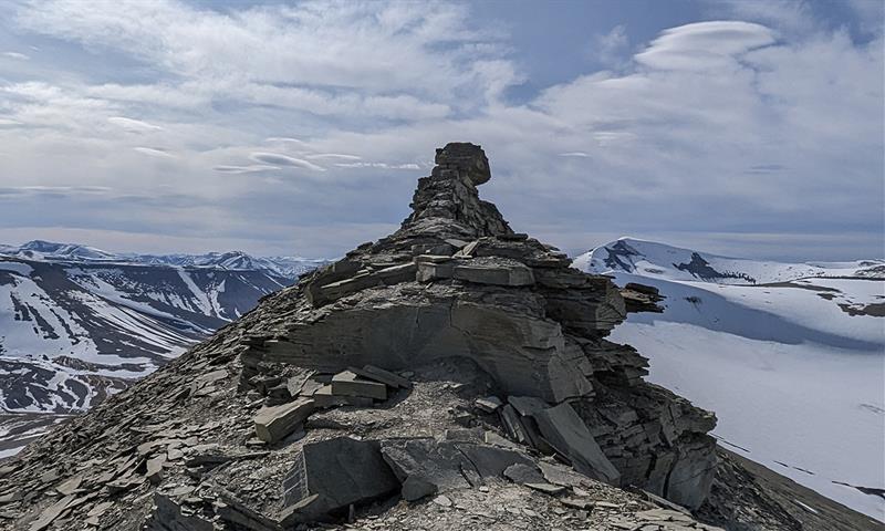 En fjellrygg med formasjonen kjent som Trollsteinen på toppen, med lett snødekte fjell og en skyet himmel i bakgrunnen