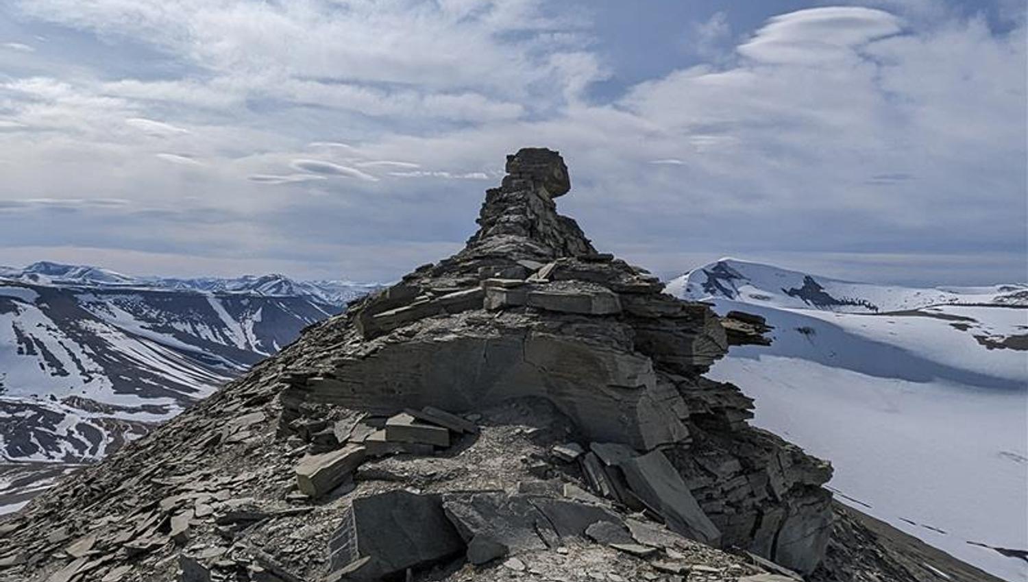 En fjellrygg med formasjonen kjent som Trollsteinen på toppen, med lett snødekte fjell og en skyet himmel i bakgrunnen