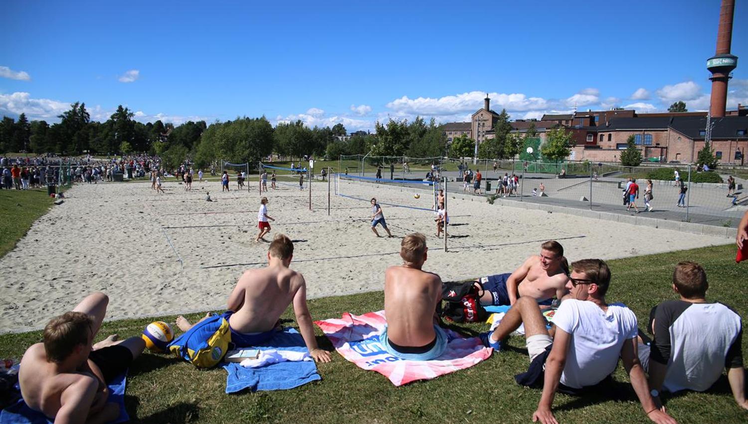 Sandvolley-bane og ungdom som sitter på gresset på siden
