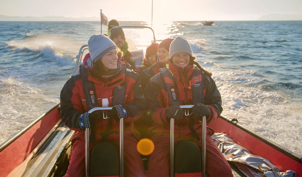 A group of guests on board a RIB boat sailing at speed in a fjord with sunshine on the fjord in the background