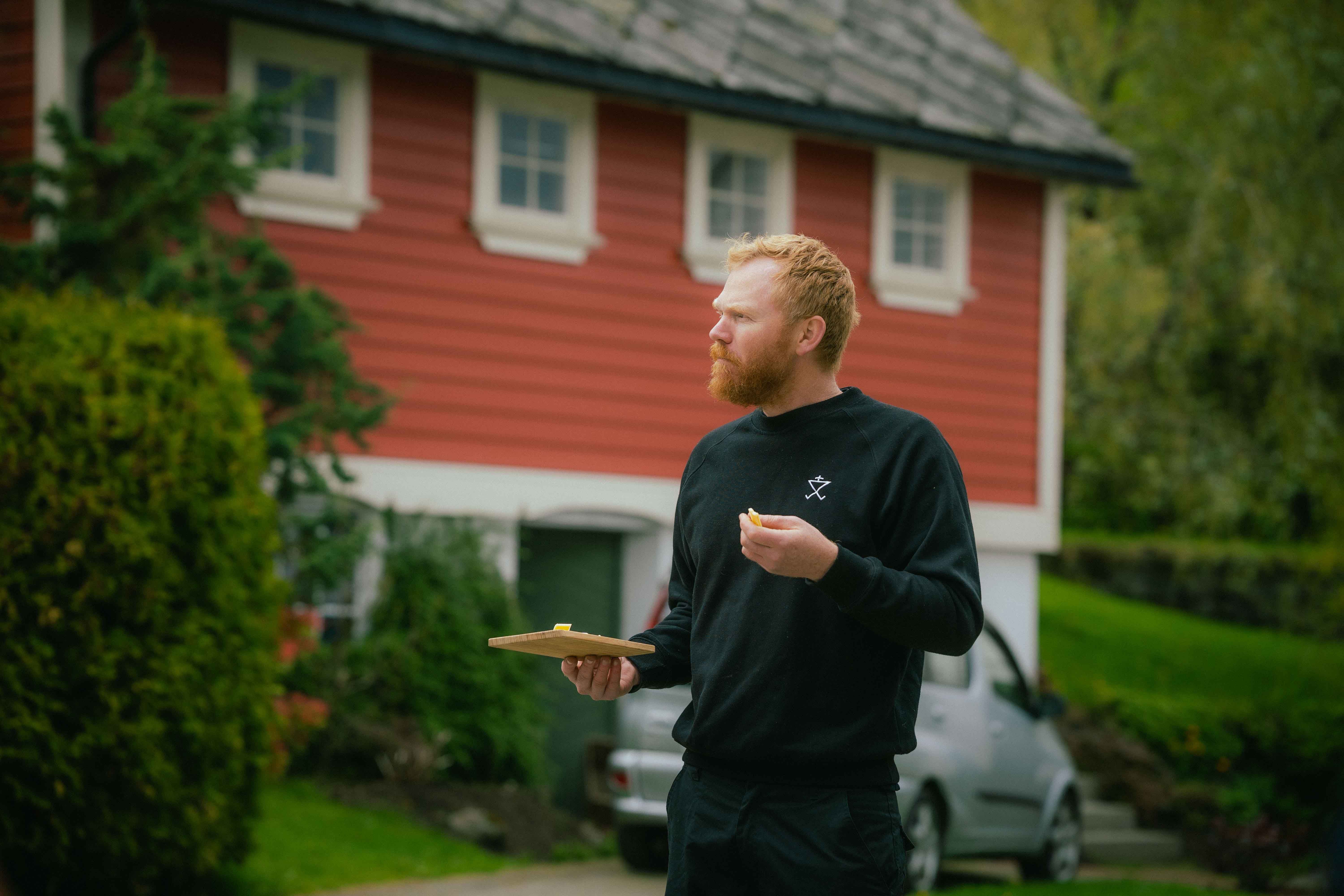 Olav Bleie frå Alde smakar på ost framfor eit tradisjonelt bygg i Hardanger.