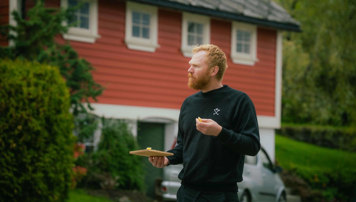 Olav Bleie frå Alde smakar på ost framfor eit tradisjonelt bygg i Hardanger.