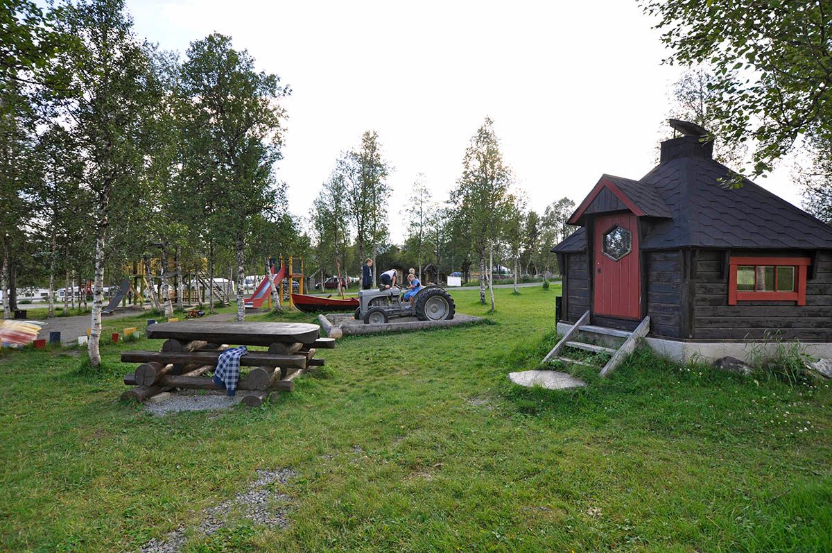Benkebord, grønn plen, lekeplass og en liten gamme