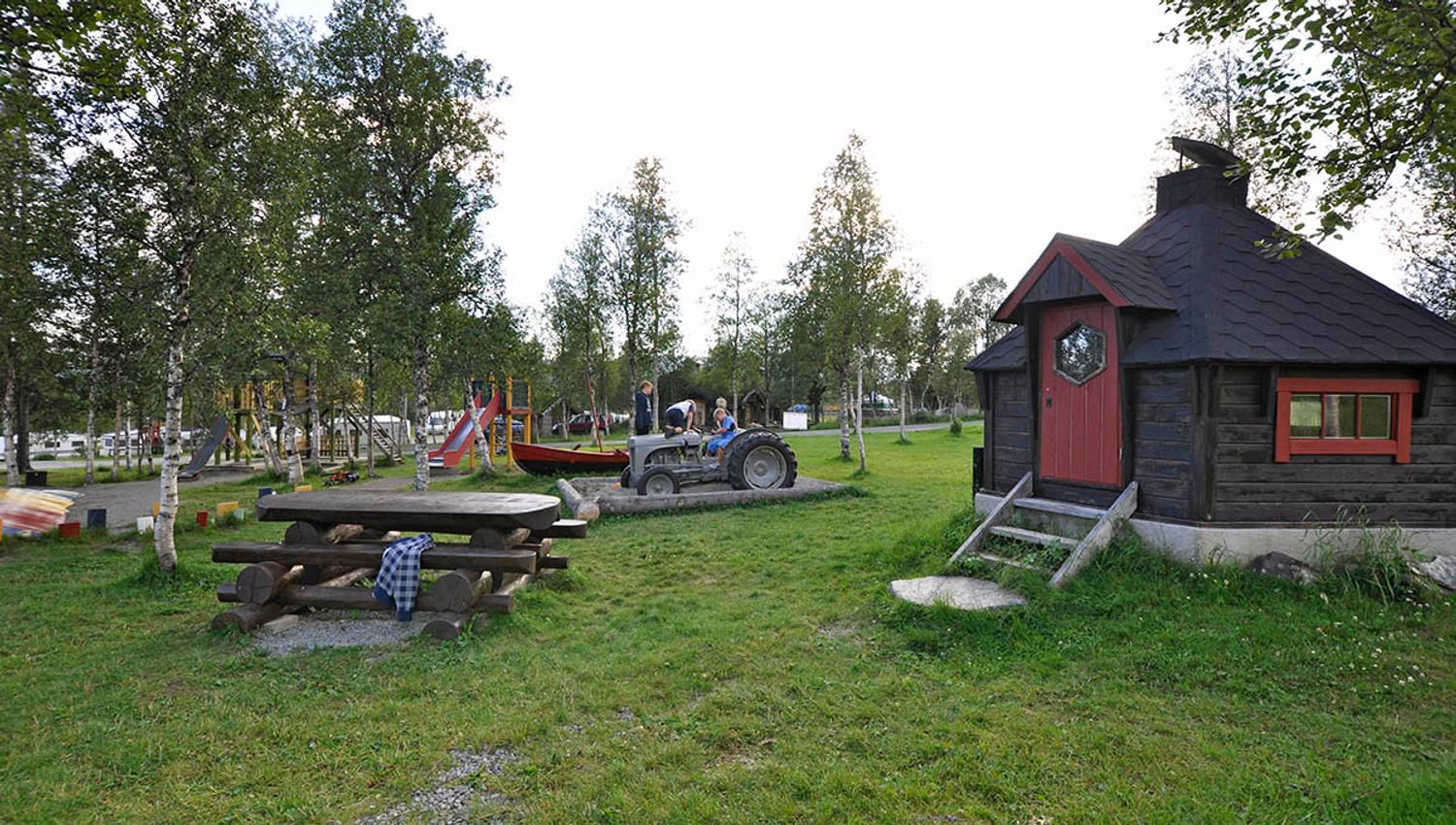 Benkebord, grønn plen, lekeplass og en liten gamme