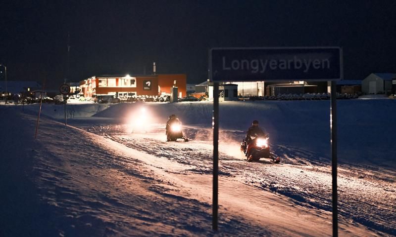 Snowmobiles driving out of the city with the Longyearbyen city sign in the front