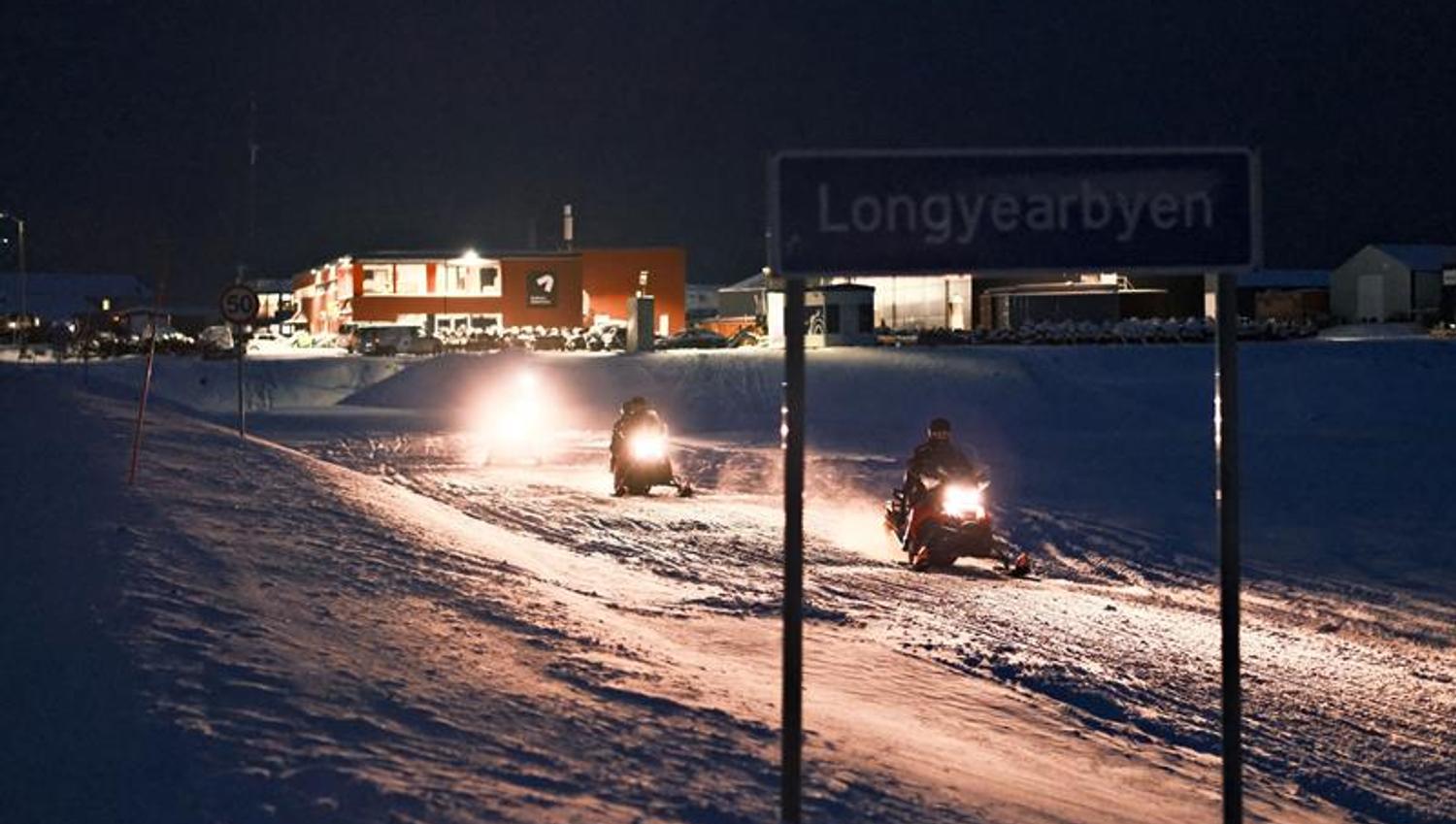 Snowmobiles driving out of the city with the Longyearbyen city sign in the front