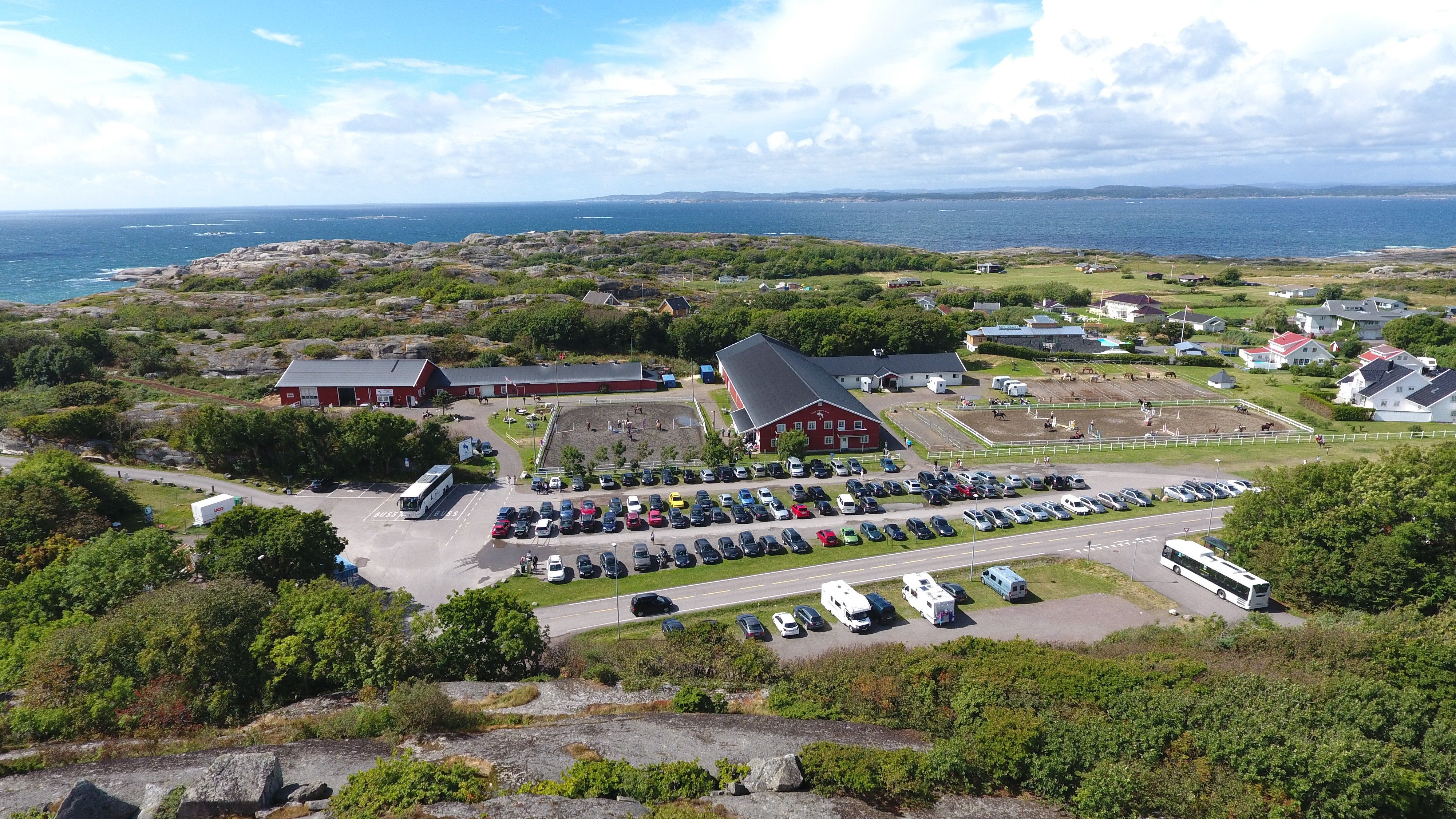 Oversiktsbilde med rød låve, parkeringsplass og sjøen i bakgrunnen.