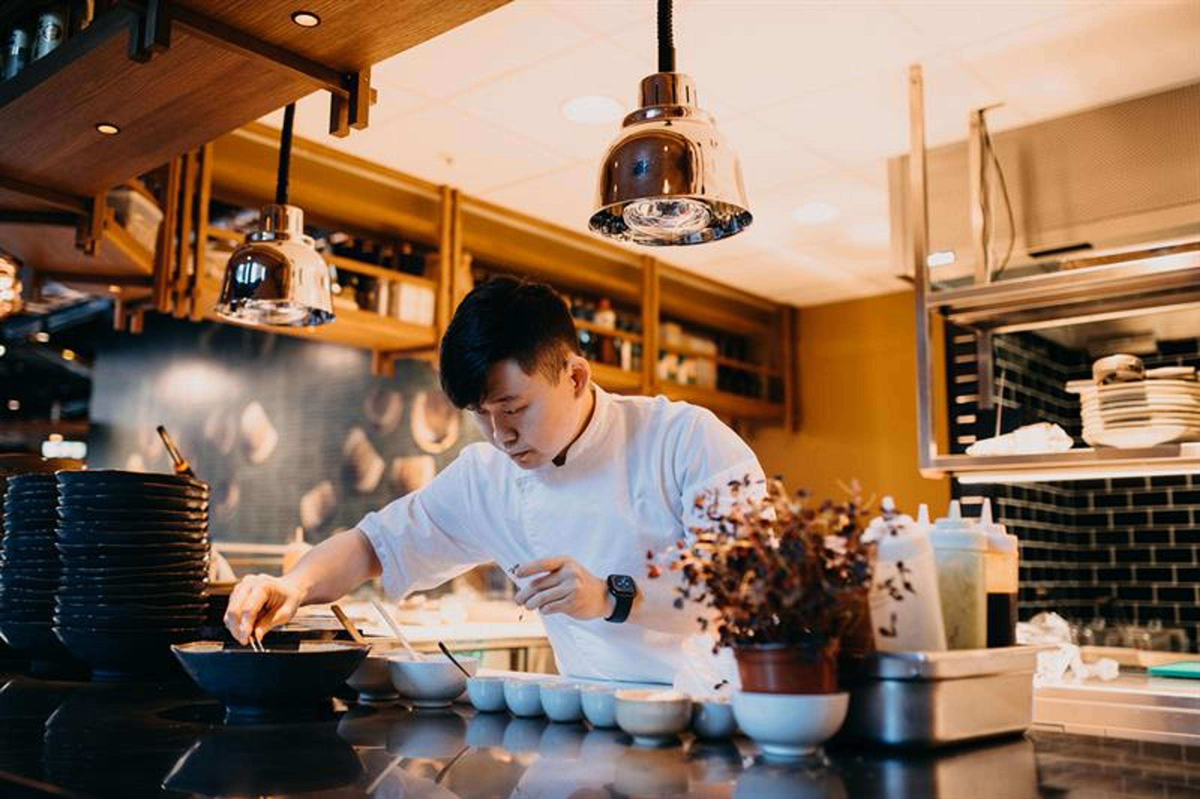A cook preparing many small dishes in white bowls