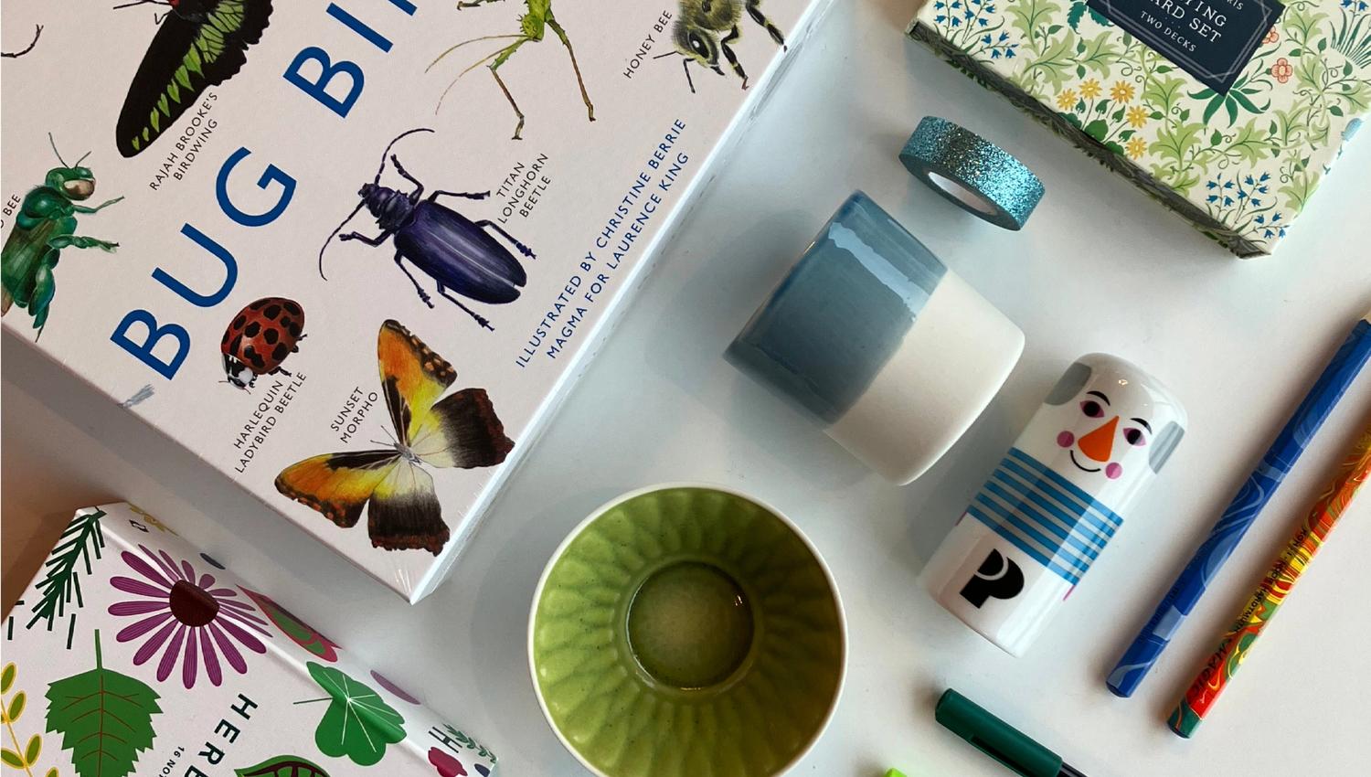 Eit utval varer frå museumsbutikken: spel, kortstokk, fargerike koppar, tusjar, blyantar og små gåveartiklar lagt ut på eit bord.