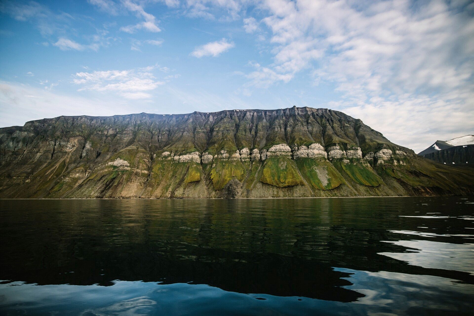 A green mountain landscape along the edge of a calm fjord