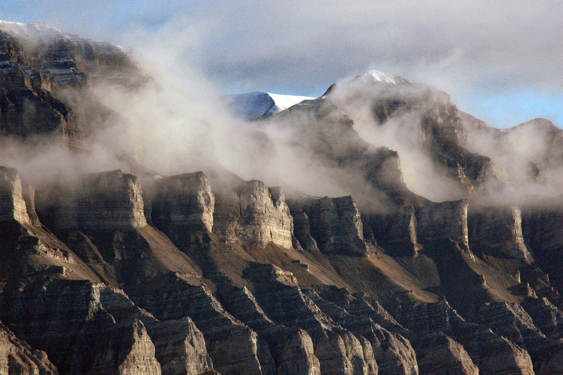 A mountain face with clouds of mist swirling in between mountain ridges along the face