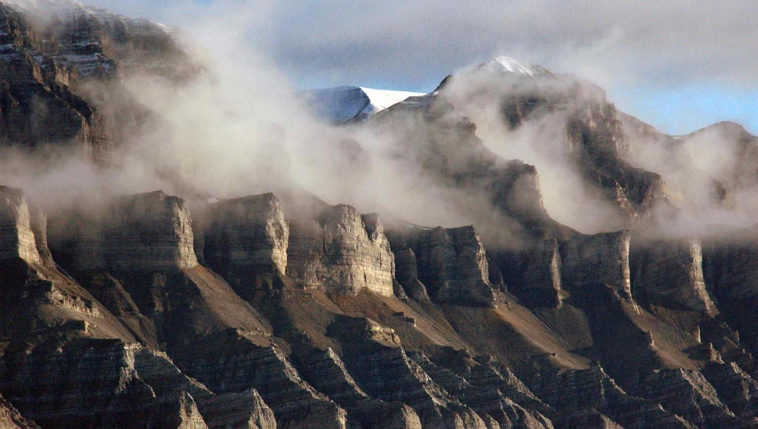 A mountain face with clouds of mist swirling in between mountain ridges along the face