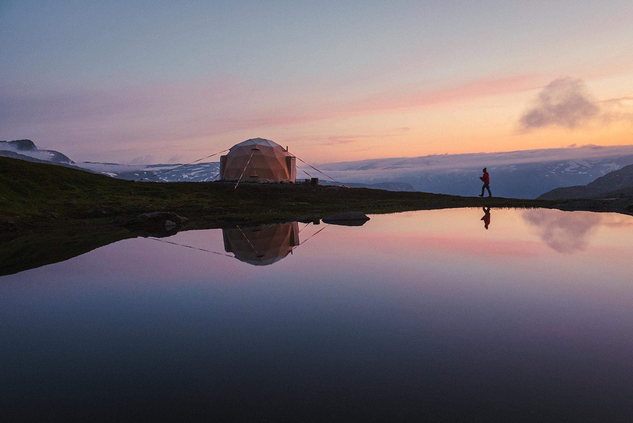 Geodesic glamping dome by a calm mountain lake at sunset near Trolltunga, Hardanger.